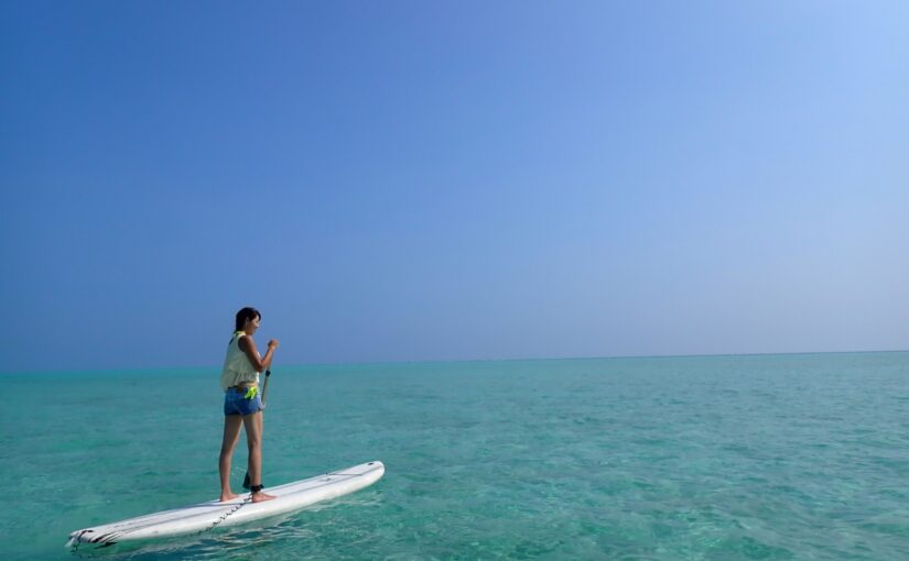 青い海と空を背景にサップ（SUP）を楽しむ女性